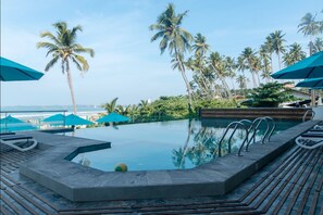 A pool area with a view of the ocean, surrounded by palm trees and blue umbrellas. - Twenty-Two Weligambay (Weligama)