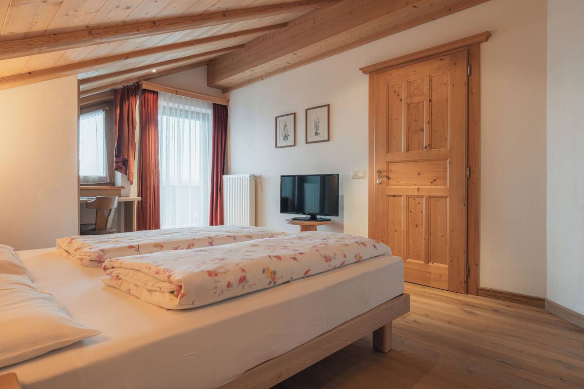 A bedroom with two beds, a TV, and a wooden wardrobe.