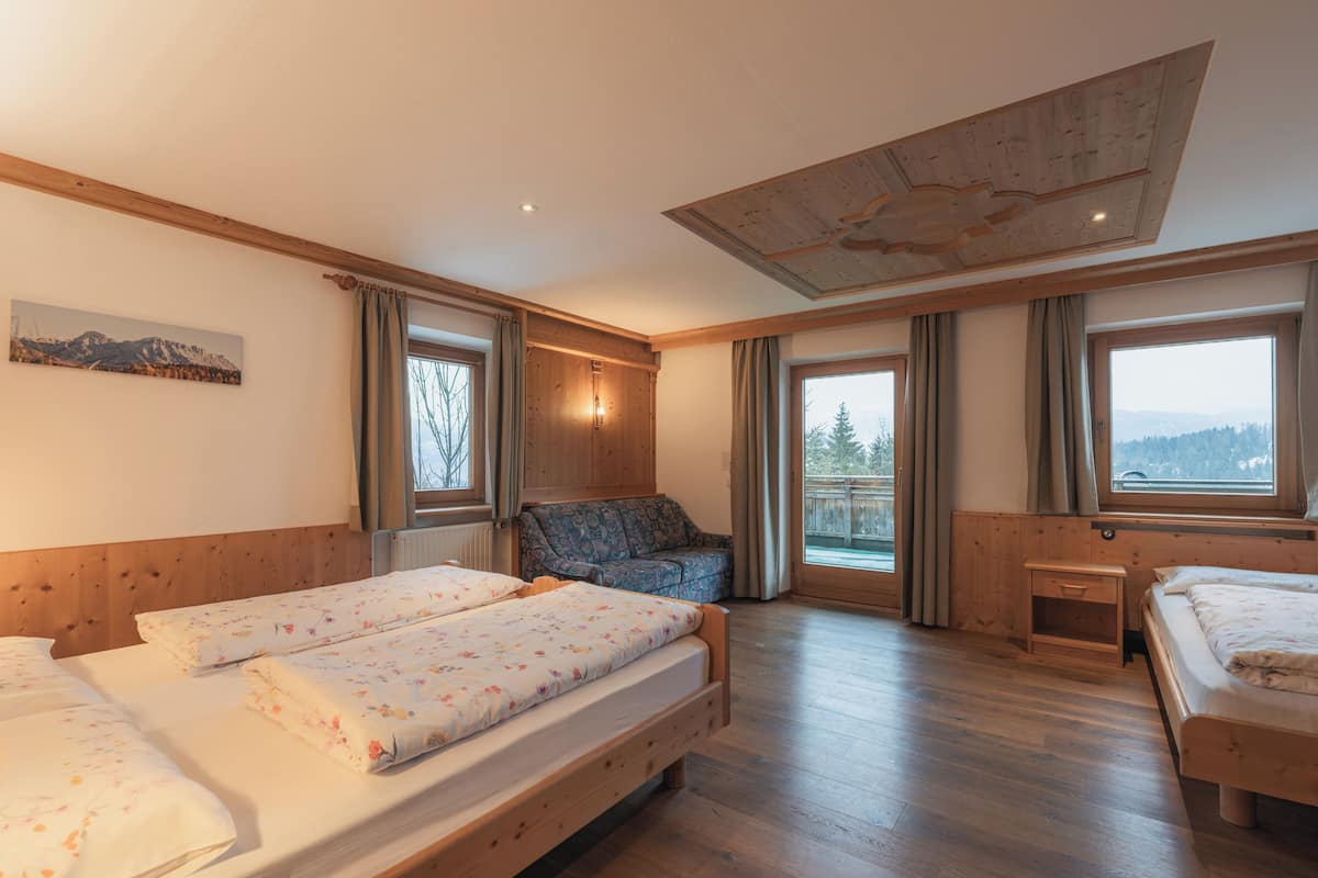 A room with two beds, a wooden ceiling, large windows, and a view of the outdoors.