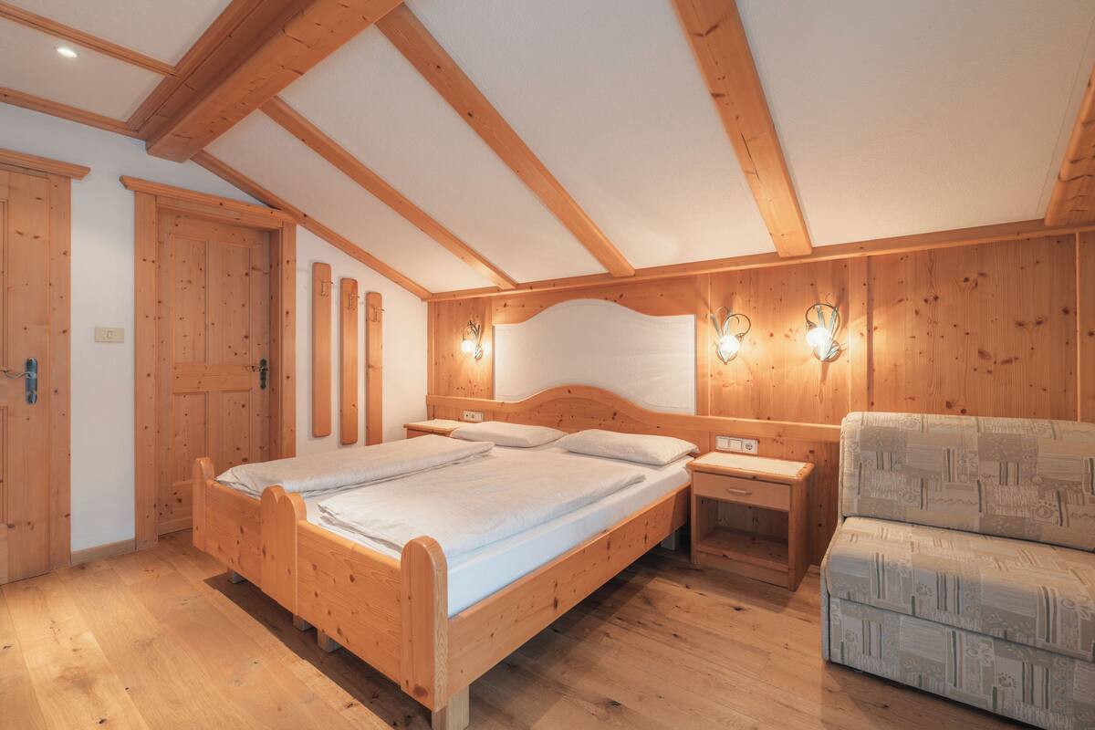 A wooden bedroom with a large bed, bedside tables, and a sofa.