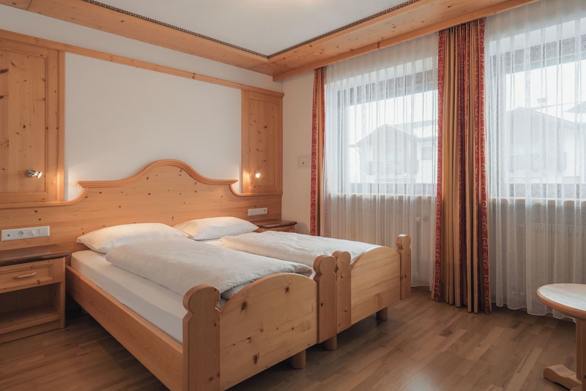 A wooden double bed with two nightstands, a wooden headboard, and a window with sheer curtains.