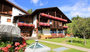 A traditional chalet with wooden balconies and flower boxes, surrounded by a well-maintained garden and a clear sky. - Pension Maria (San Martino in Badia)
