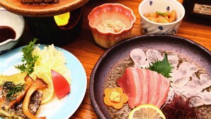 Diversos platos, como sashimi, carne a la parrilla y verduras, sobre una mesa de madera.