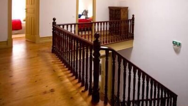 A spacious room with wooden flooring, a staircase with a black railing, and a modern light fixture on the ceiling. - A Vianesa Guest House (Viana do Castelo)