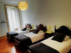 A hotel room with two single beds, a wooden floor, a large window with curtains, and a hanging light fixture. - A Vianesa Guest House (Viana do Castelo)