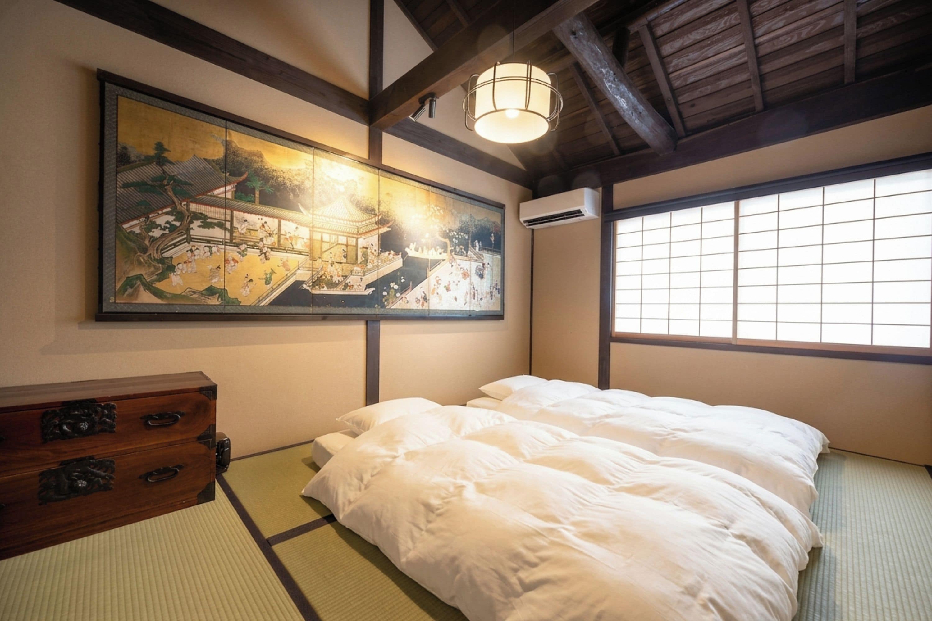 A traditional Japanese room with tatami flooring, a bed with white bedding, a wooden dresser, and a large painting of a historical scene.