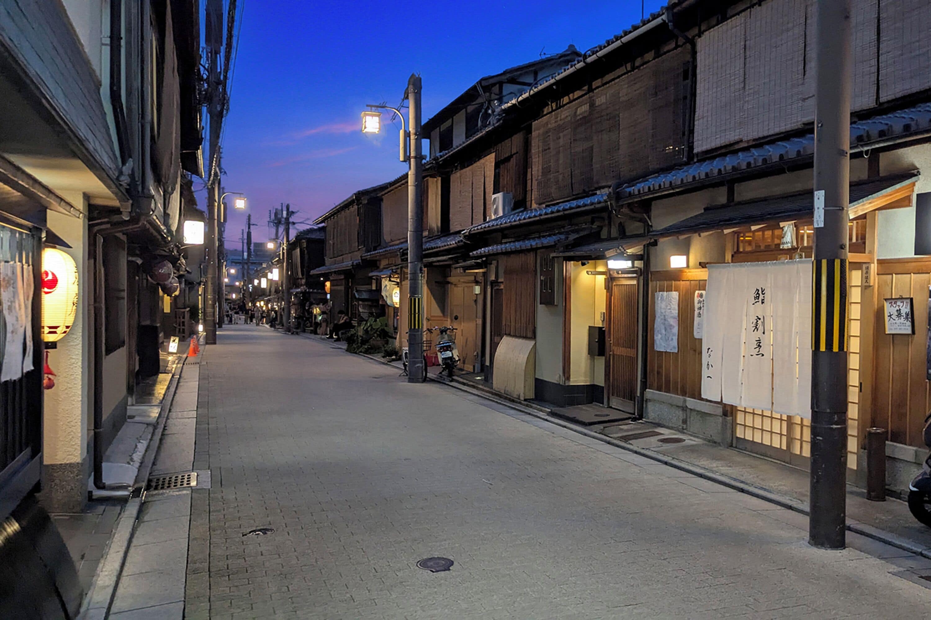 A narrow street lined with traditional wooden buildings, some with signage, and a few bicycles parked along the side.