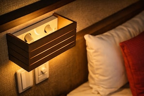 Una lámpara de pared con estructura de madera, almohada blanca y manta roja sobre una cama.