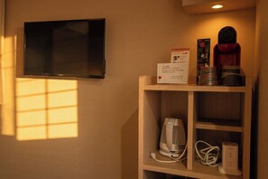 Une chambre d’hôtel équipée d’un téléviseur à écran plat fixé au mur, d’une étagère en bois sur laquelle se trouvent une machine à café, une bouilloire et une multiprise.