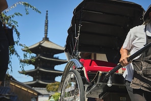 Un rickshaw tradicional con una cubierta roja, una persona sosteniendo el manillar y una pagoda al fondo.