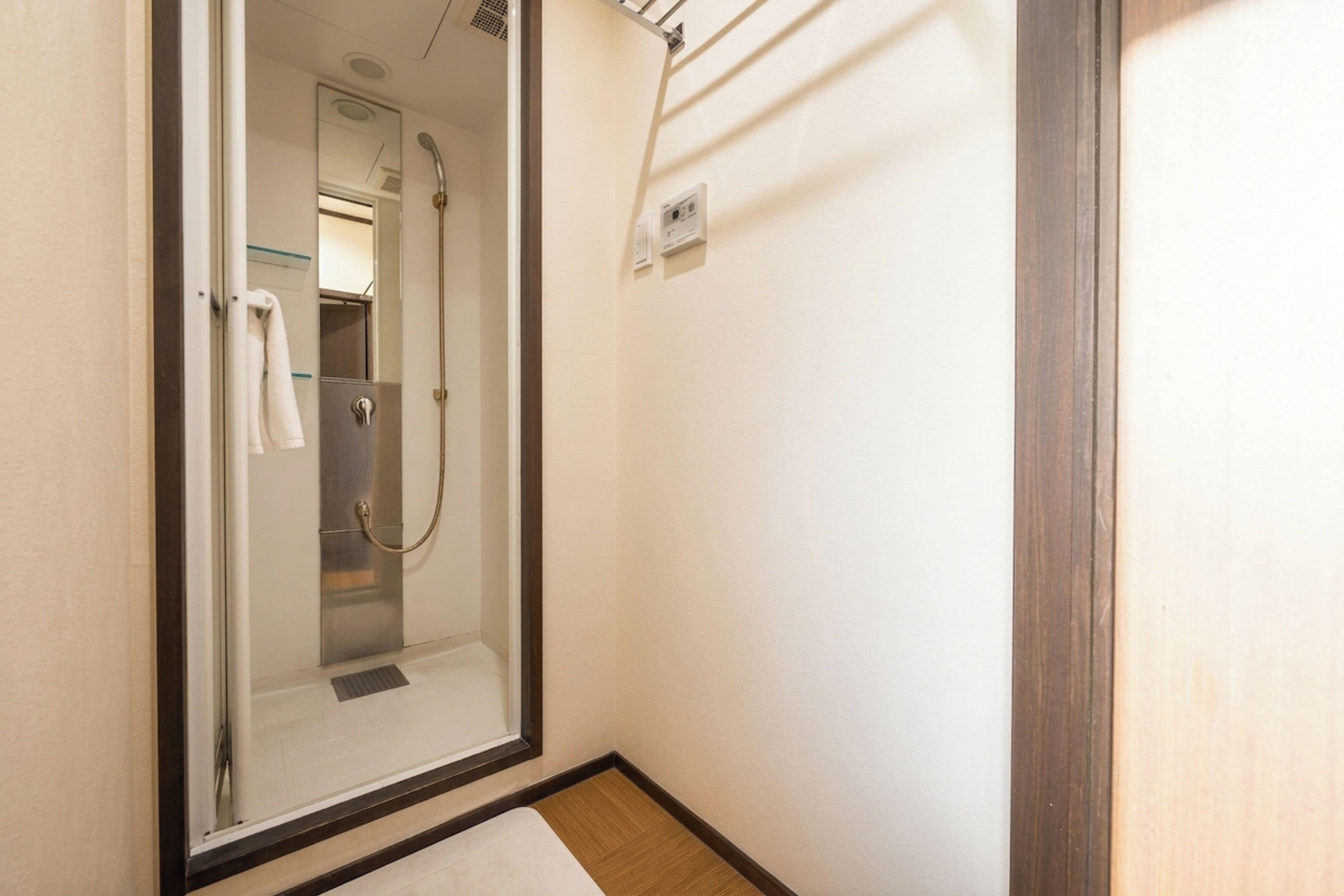 A glass-enclosed shower stall with a towel rack and a control panel on the wall.