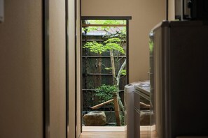 Een smalle gang met een houten vloer die leidt naar een traditionele Japanse tuin met een bamboe en een steen.