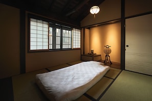 A traditional Japanese room with tatami flooring, a futon bed, a shoji screen window, and a hanging lantern.