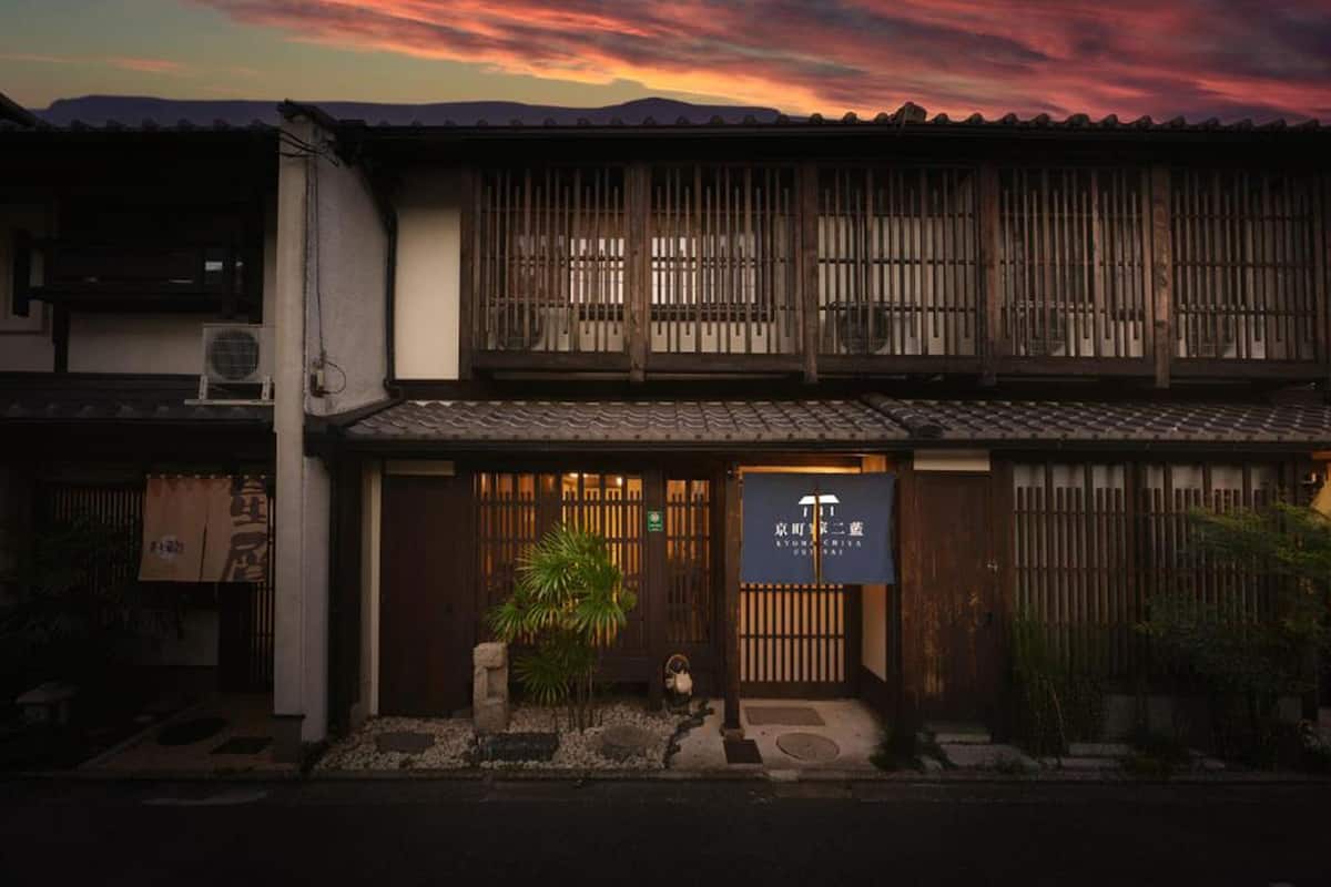A traditional Japanese building with a wooden gate, a small garden, and a signboard.