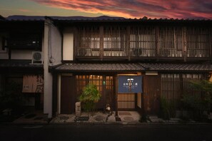 A traditional Japanese building with a wooden gate, a small garden, and a signboard.