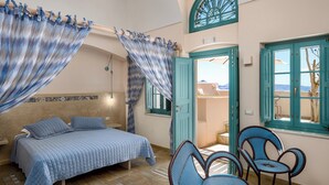 A bedroom with a bed, two chairs, a window with a view, and a door leading to a balcony. - Passion Blue Villas (Santorini)