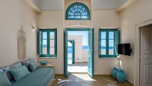 A room with a sofa, a small table, and a TV on the wall. - Passion Blue Villas (Santorini)