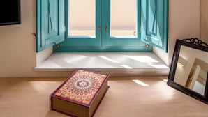 A room with a window featuring teal shutters, a wooden desk, and a framed picture. - Passion Blue Villas (Santorini)