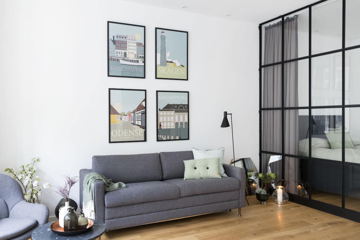 A modern living room with a grey sofa, a coffee table, and framed cityscape pictures on the wall.