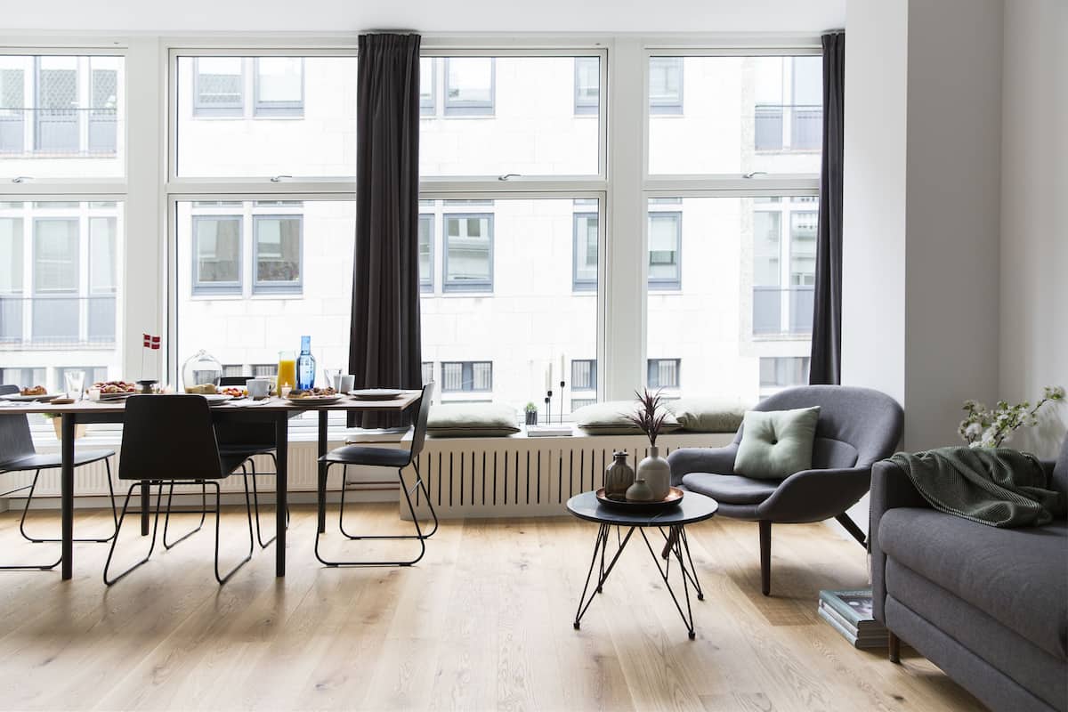 A modern living room with a dining area, large windows, and a view of buildings.