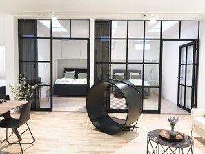 A modern hotel room with a large bed, a hanging chair, a dining area with a table and chairs, and large windows with curtains. - The Nordic Collection V (Copenhagen)