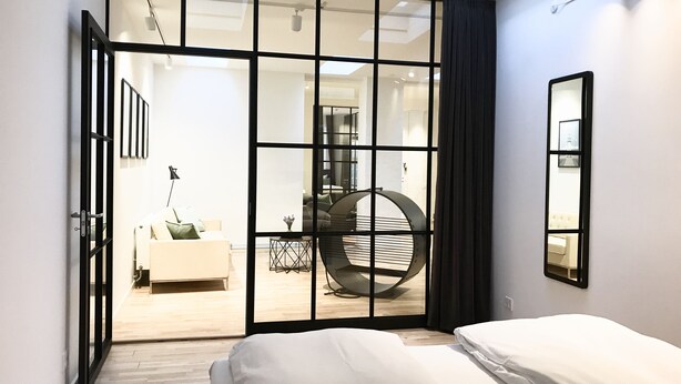 Un dormitorio moderno con una cama grande, un puerta corrediza de vidrio que da a una sala de estar y un tragaluz.