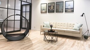 Una sala de estar moderna con un sofá, una silla negra redonda, una mesita y cuadros con vistas de la ciudad en la pared.