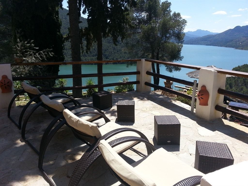 Eine Terrasse mit Korbmöbeln, Blick auf einen See und Berge im Hintergrund.