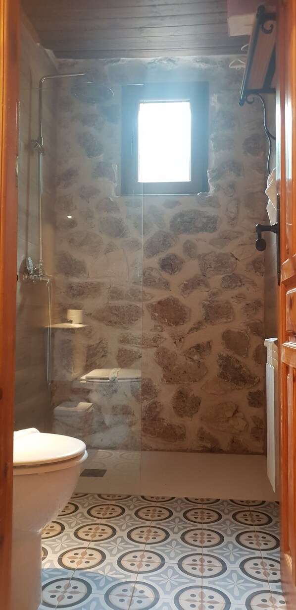 A bathroom with a stone wall, a toilet, and a shower area.