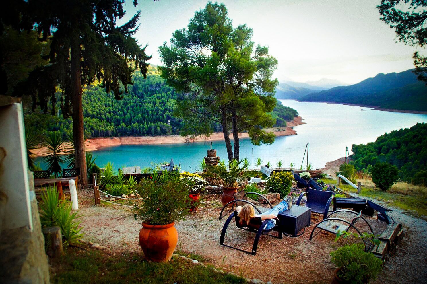 Un patio con mobiliario exterior, vista a un lago y follaje circundante.