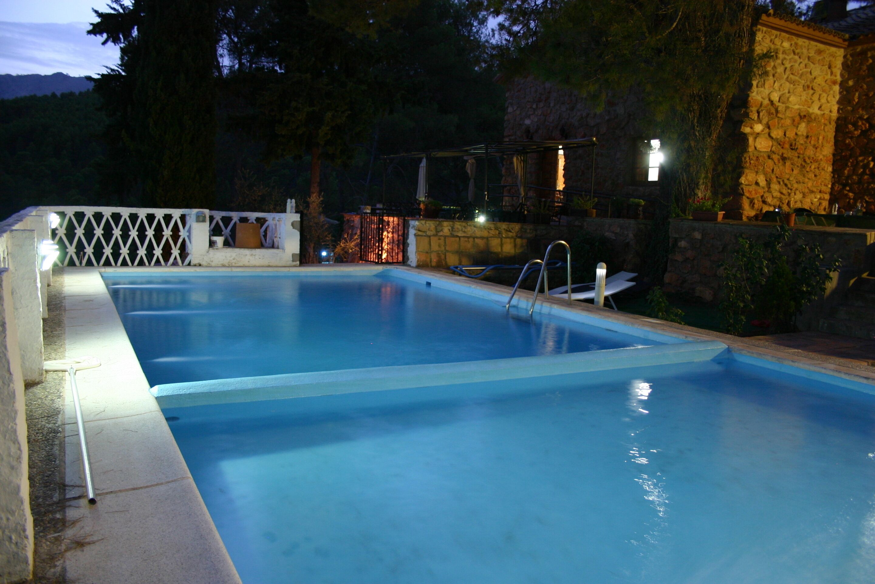 A rectangular swimming pool with a white fence and a stone wall in the background.