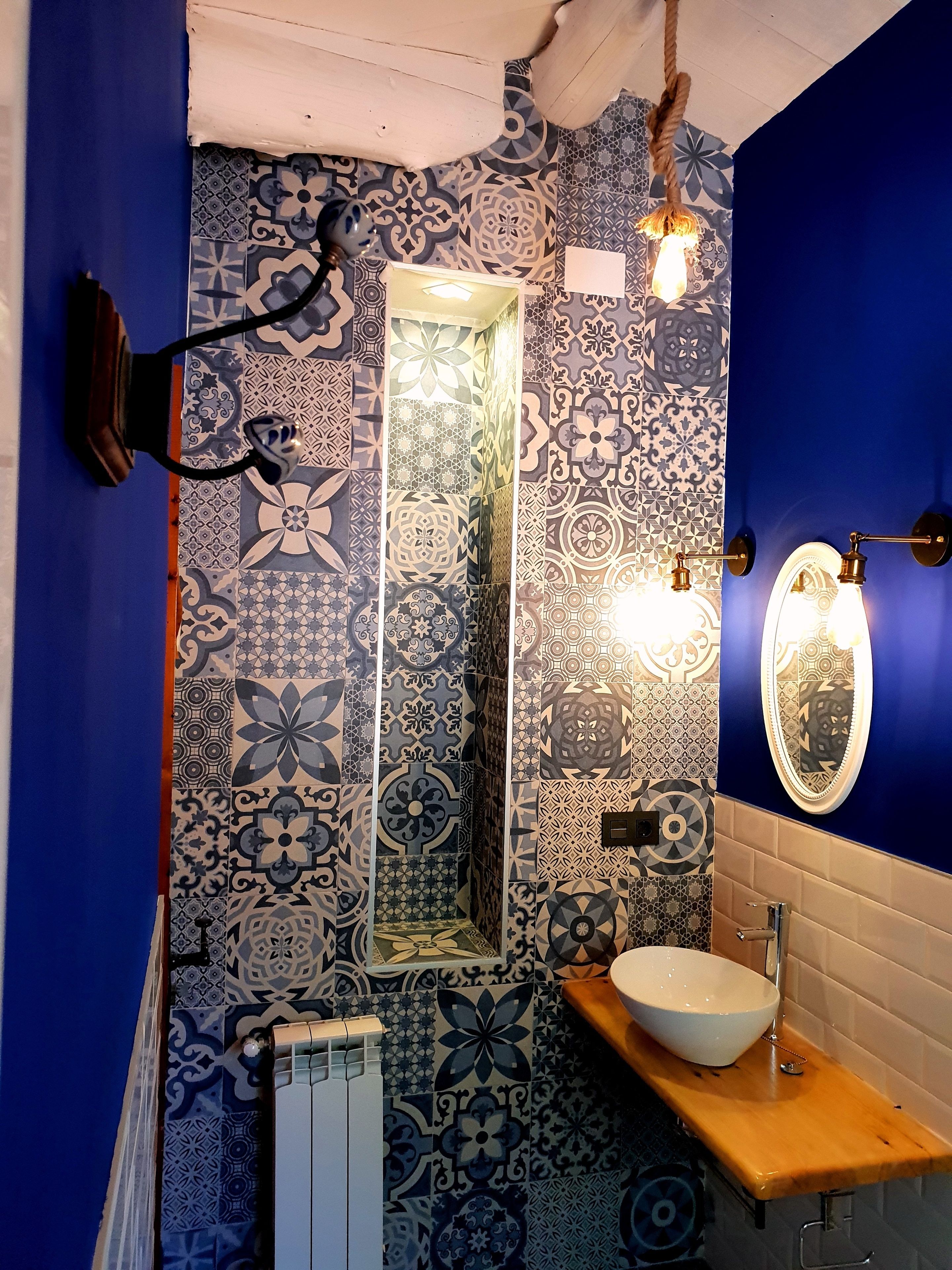 Un baño con paredes azules, baldosas estampadas, un lavabo blanco y un espejo con marco decorativo.