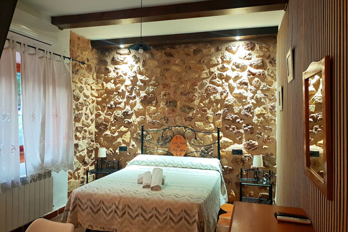 Ein Schlafzimmer mit einer Steinsäule, einem Bett mit aufgerollten Handtüchern, einem Nachttisch mit Lampe und einem Holztisch.