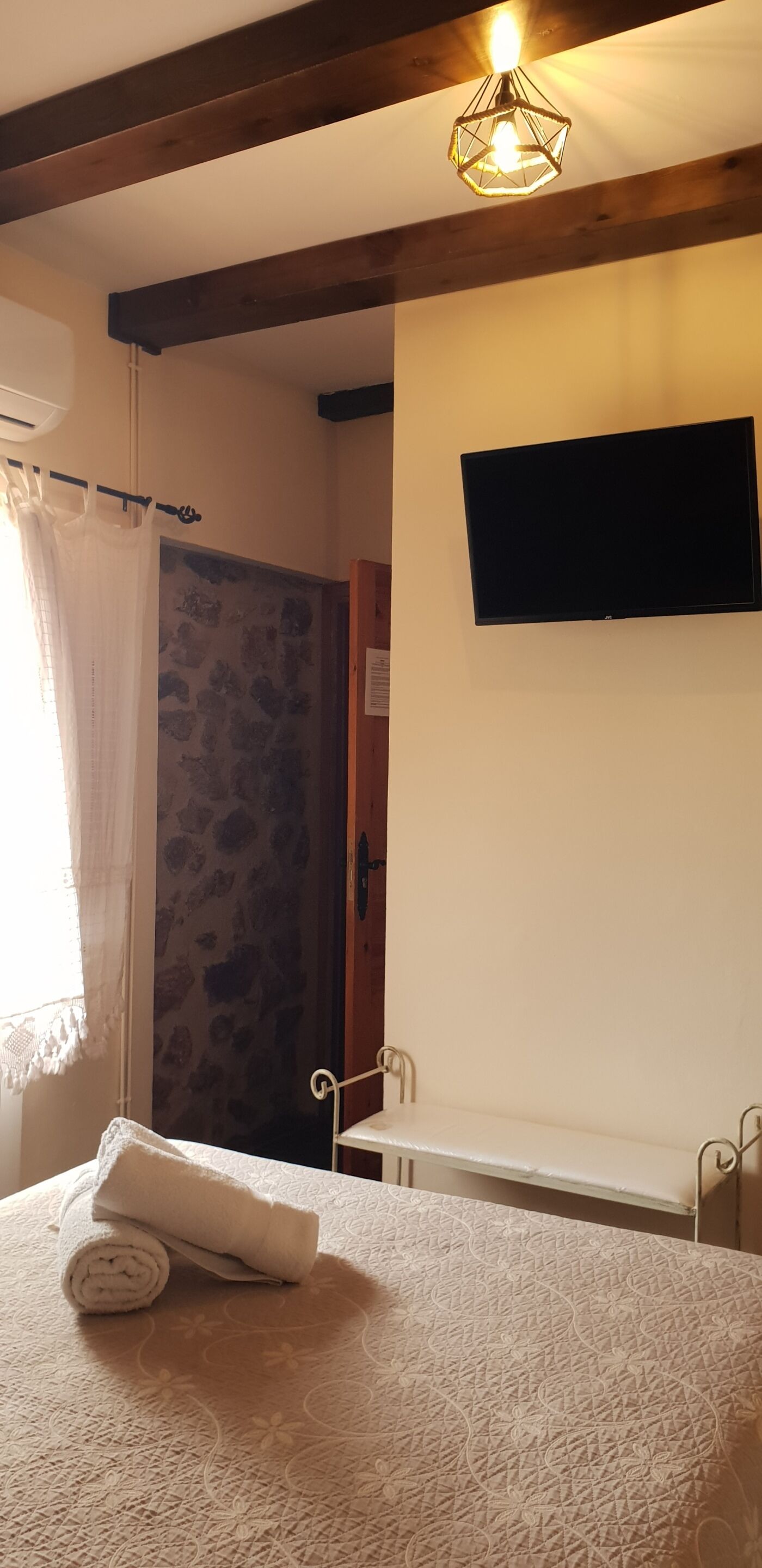 Een slaapkamer met een bed, een televisie, een douche en een raam met gordijn.
