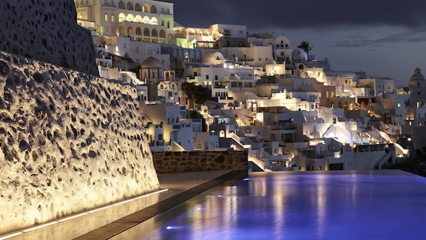 A coastal town with white buildings, a stone wall, and a reflective pool. - Villa Bordeaux (Santorini)