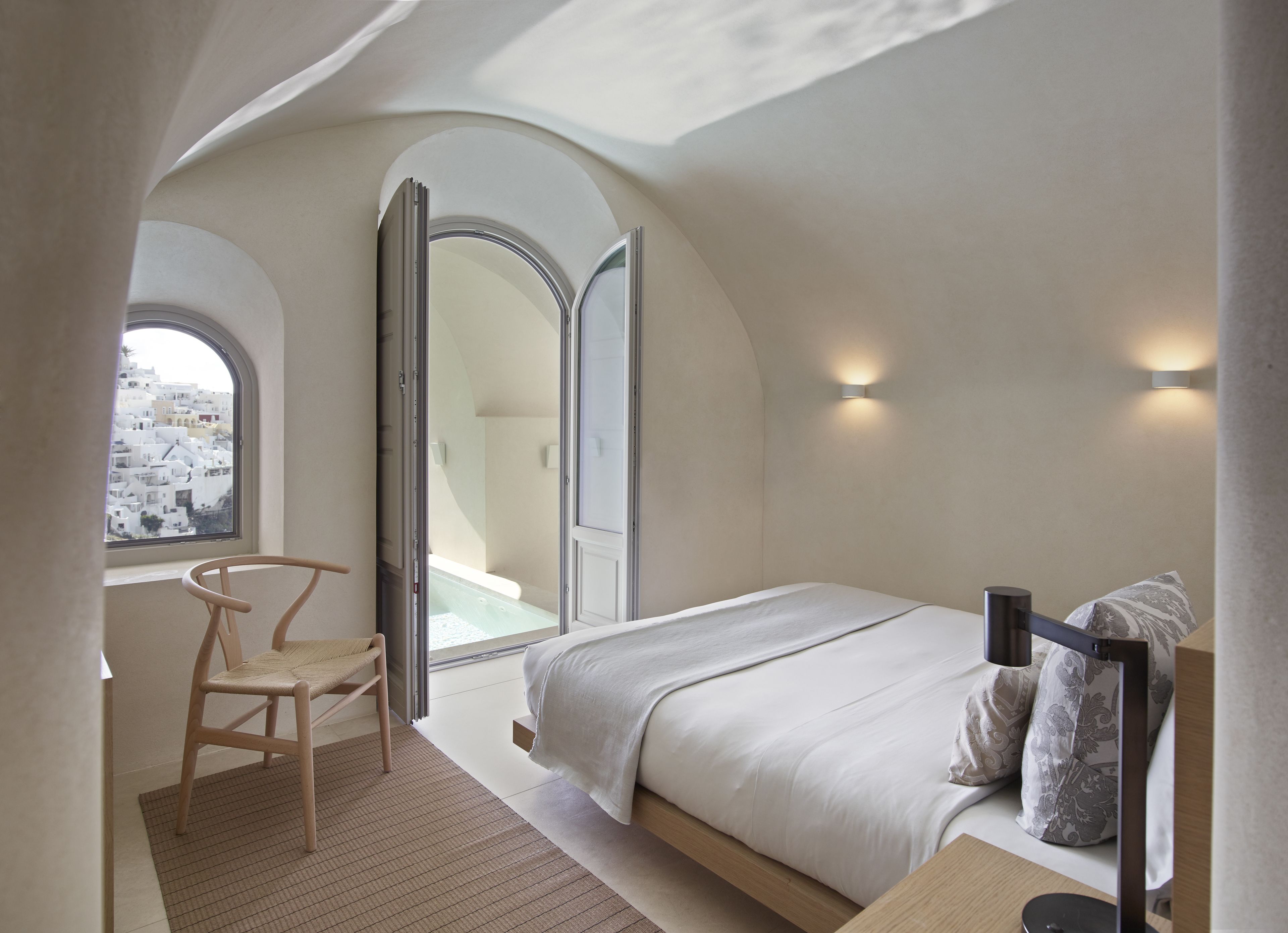 Un dormitorio con cama, una silla, un ventanal y vistas a un balcón.