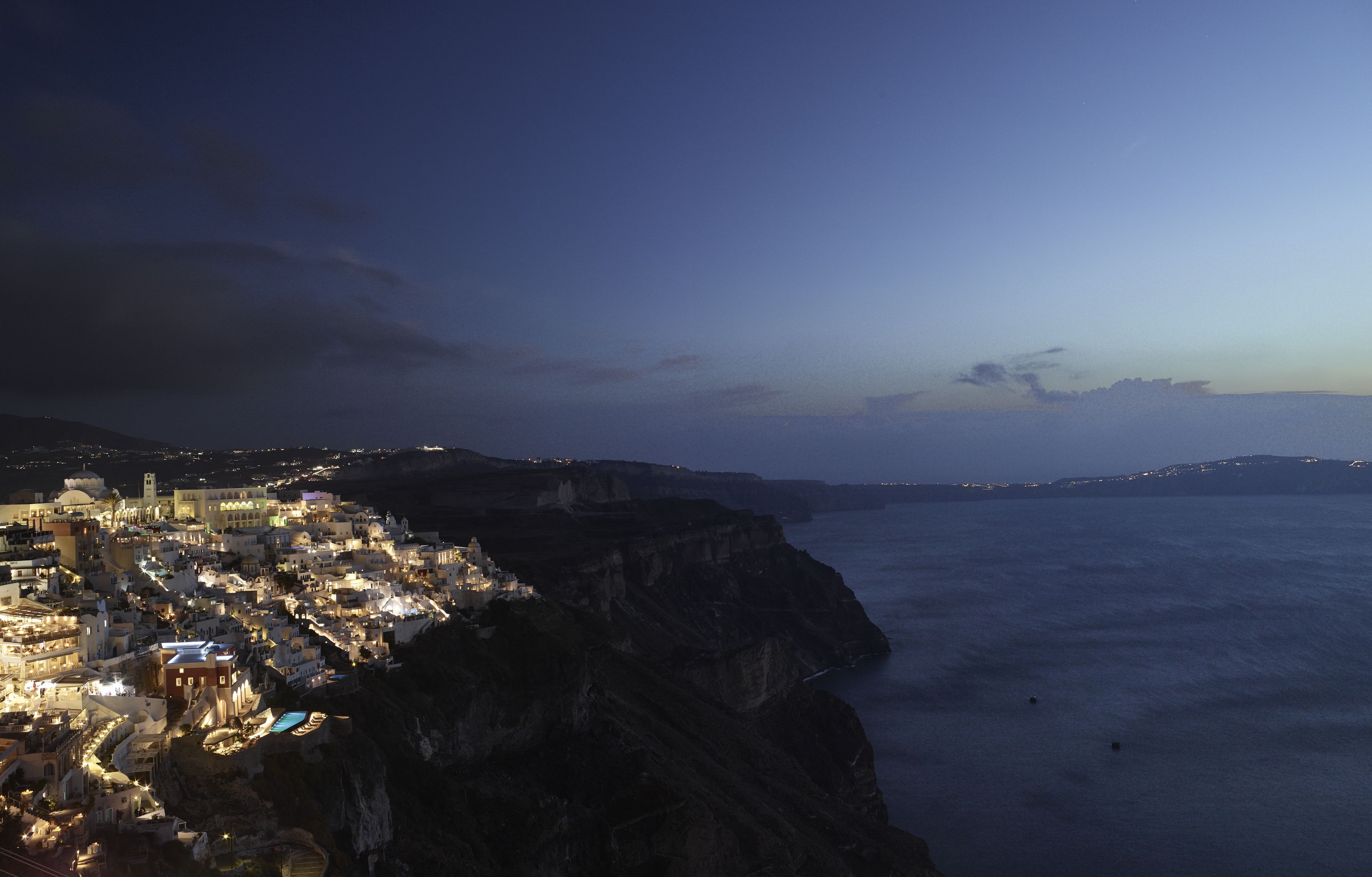 Un pueblo costero de noche con edificios a lo largo del acantilado y vista al mar.