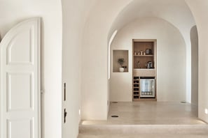 A minimalist hallway with a white door, a wooden cabinet with kitchenware, and a plant.