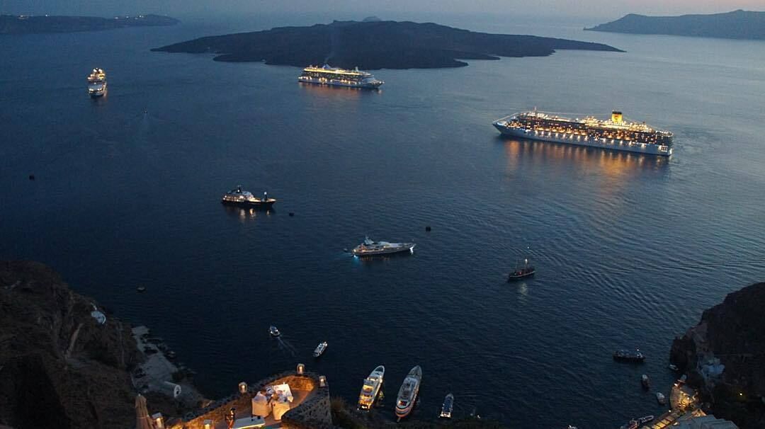 Un gran crucero amarrado en un puerto, con varias embarcaciones más pequeñas cerca.