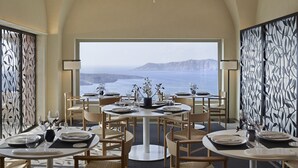 A dining area with round tables, wooden chairs, and a view of the sea. - Villa Bordeaux (Santorini)