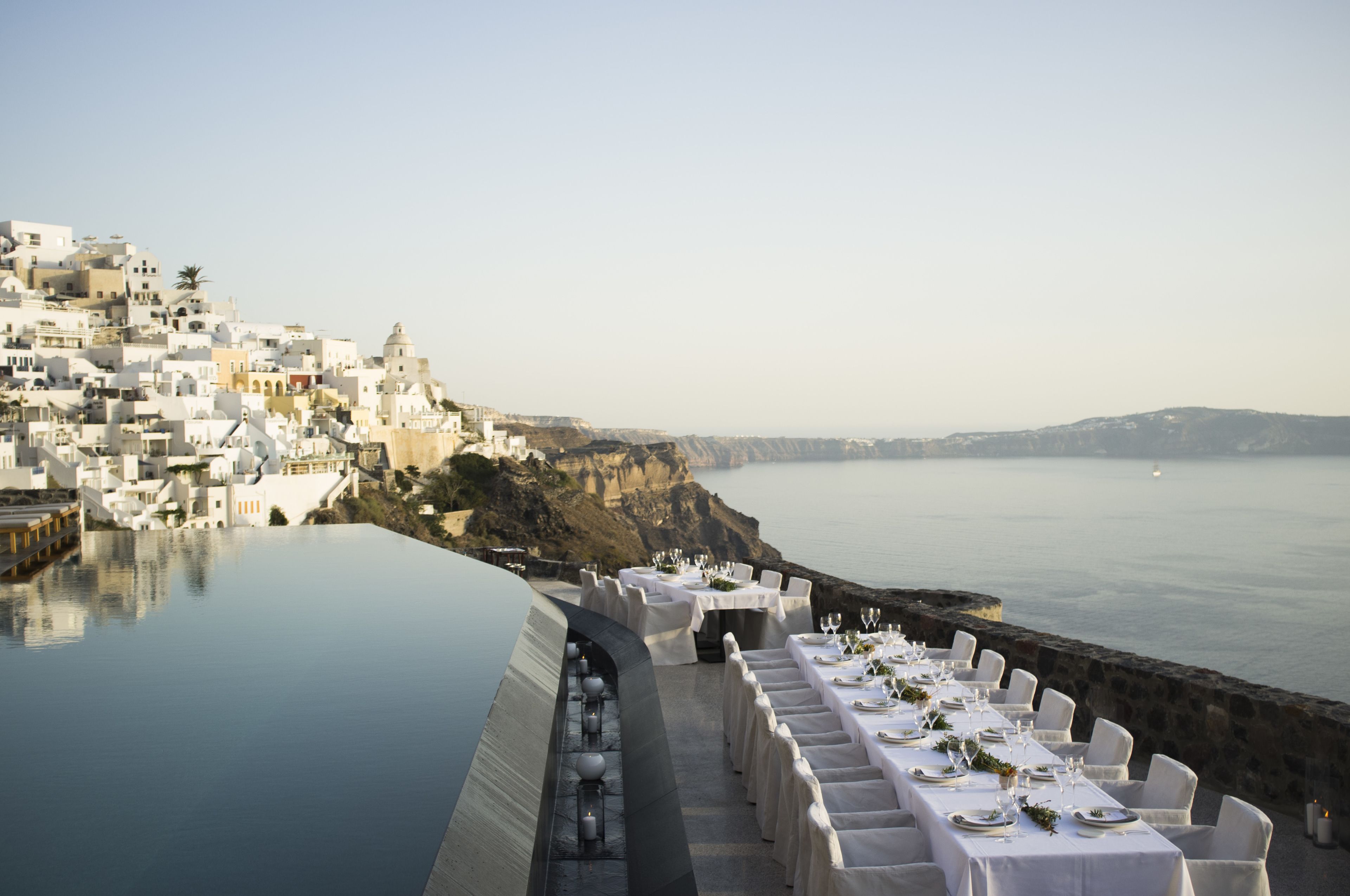 A seaside restaurant with white tables set for dining, overlooking a cliff and the sea.