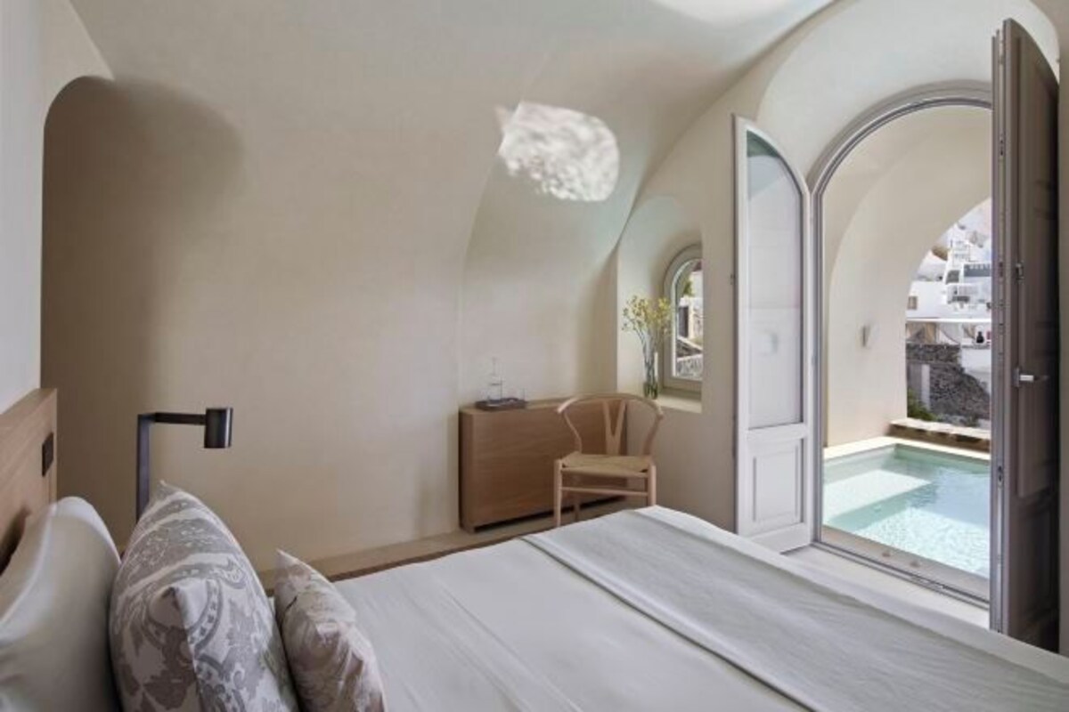A bedroom with a bed, a chair, a bedside table, and a view of a swimming pool.