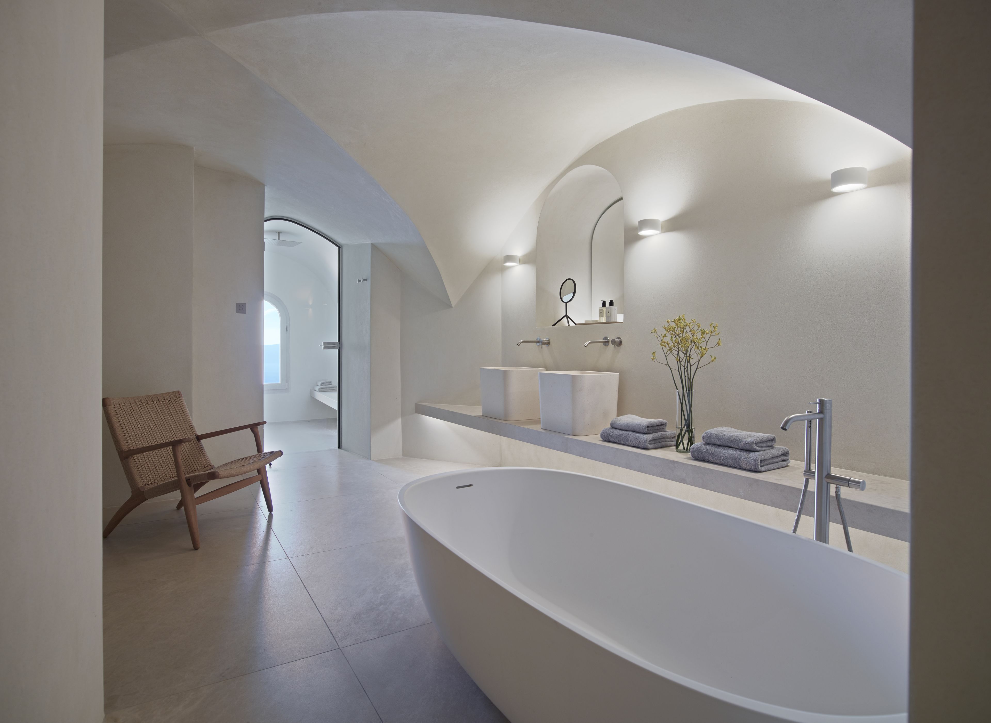 A modern bathroom with a freestanding bathtub, a large mirror, and a wooden chair.