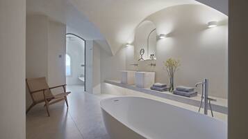 A modern bathroom with a freestanding bathtub, a large mirror, and a wooden chair.