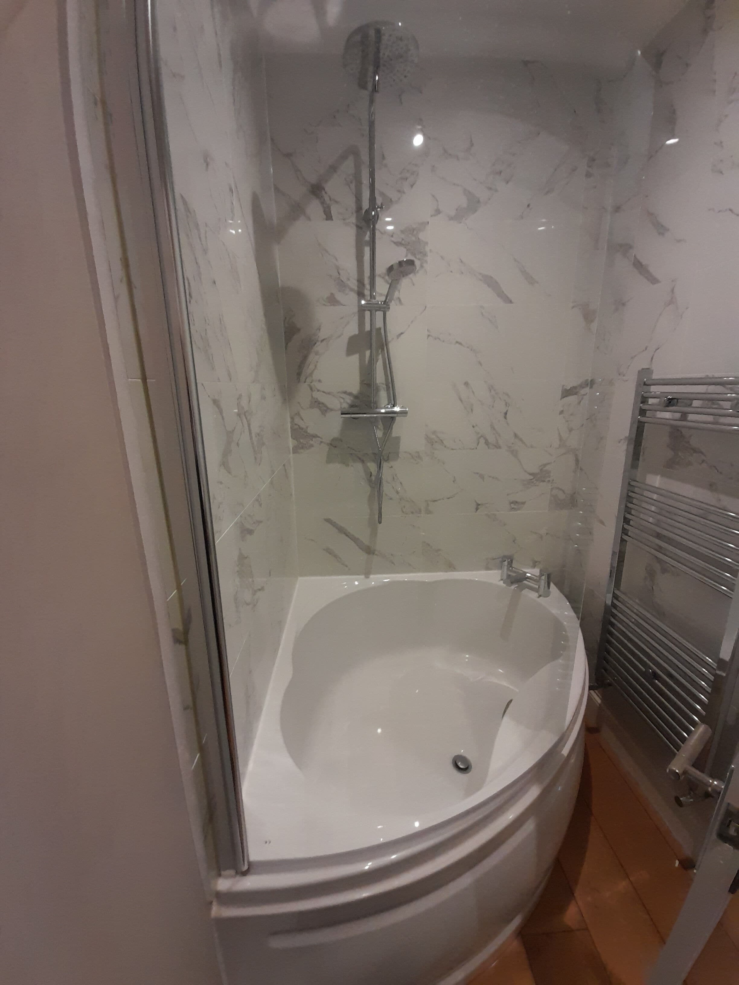 Ett badrum med ett badkar som är omgivet av glasväggar, ett duschmunstycke och en handduksställning.