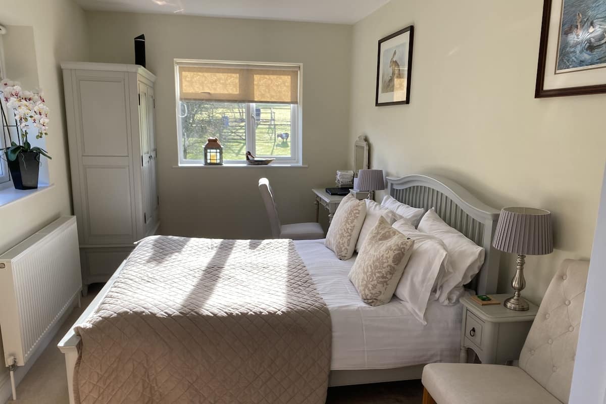 A bedroom with a bed, bedside tables, a chair, a window with a view of the outside, and a radiator.