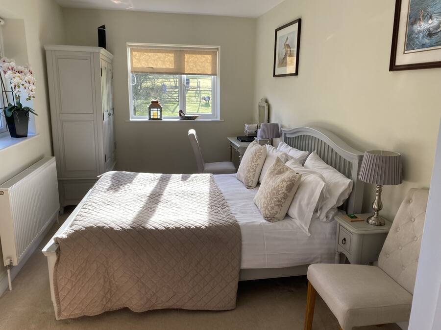 Une chambre à coucher comprenant un lit, des tables de chevet, une chaise, une fenêtre donnant sur l’extérieur et un radiateur.
