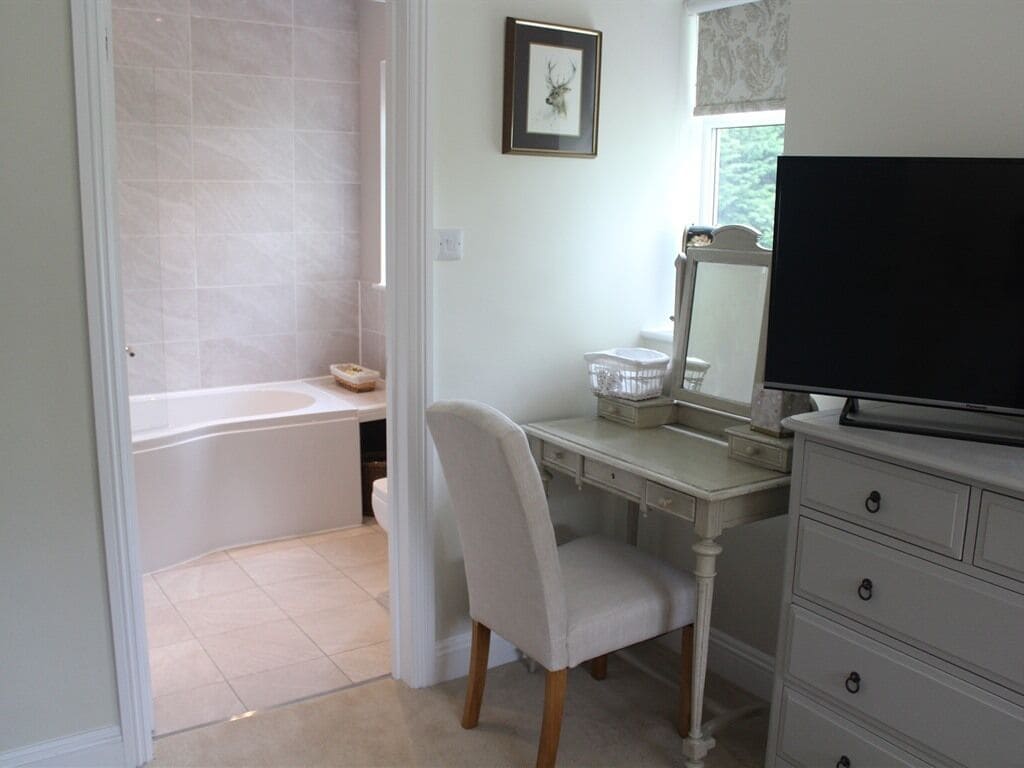 A bathroom with a bathtub, a vanity with a mirror, and a chair.