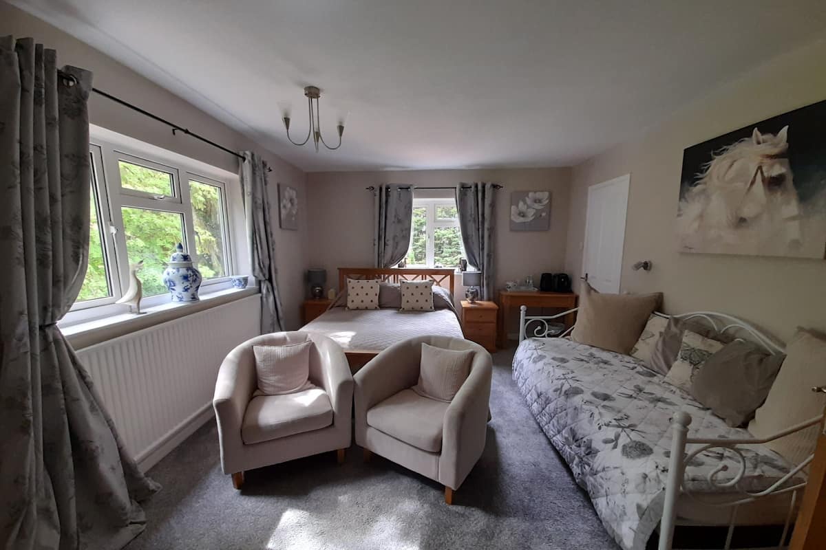 A bedroom with a bed, two armchairs, a desk, and a painting on the wall.
