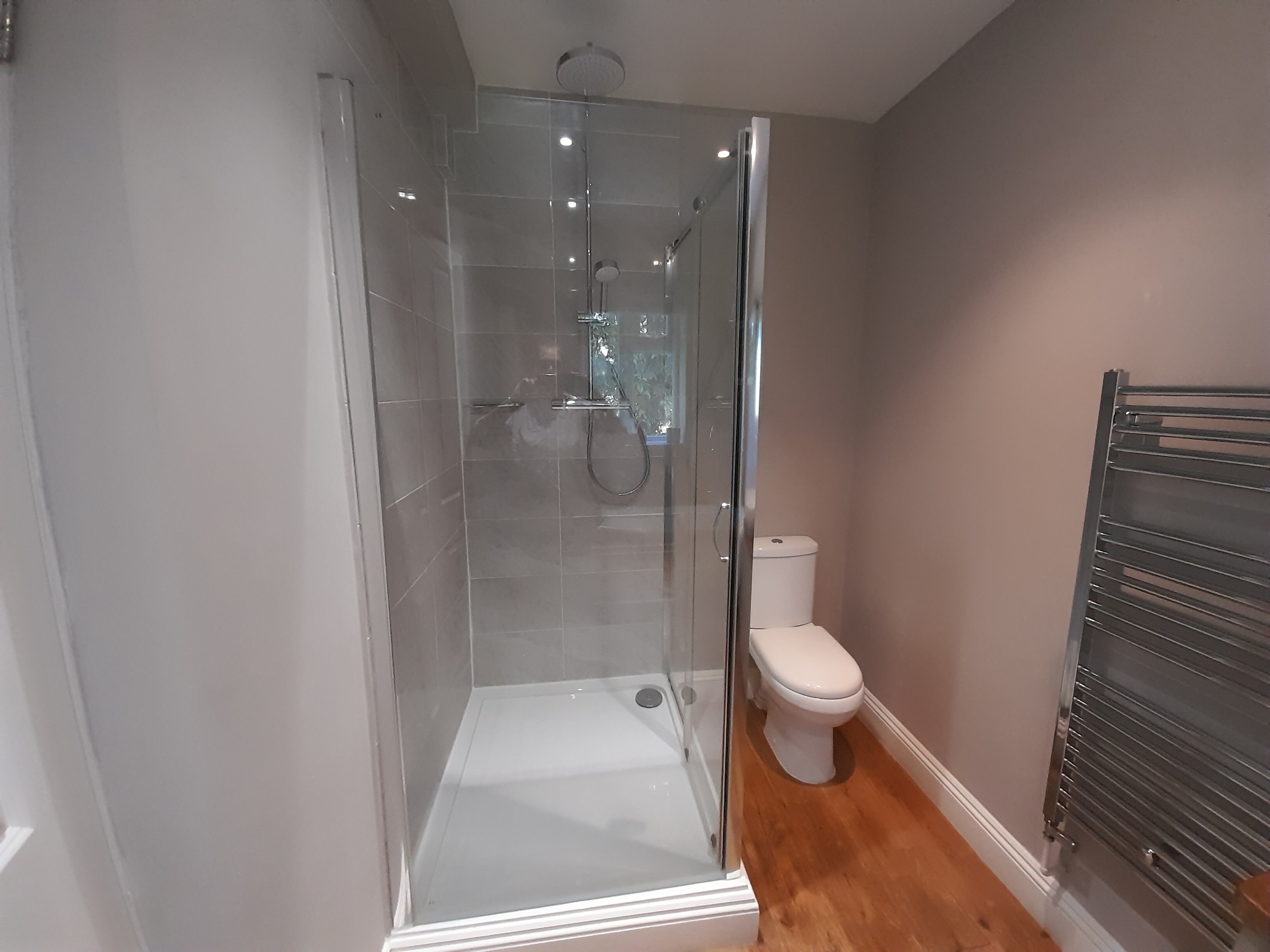 Un baño moderno con cabina de ducha de vidrio, un inodoro blanco y un perchero metálico.